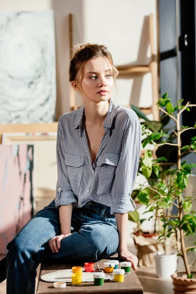 Young female artist sitting on bench with paints and looking away — Stock Photo