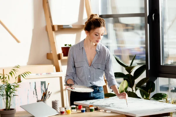 Female artist with palette drawing picture by paintbrush — Stock Photo