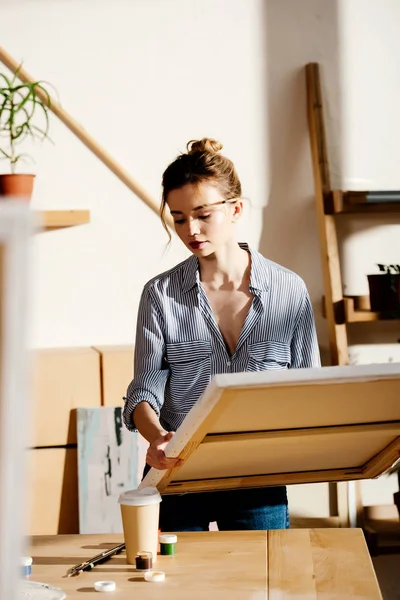 Young female artist with canvas in hands in art studio — Stock Photo