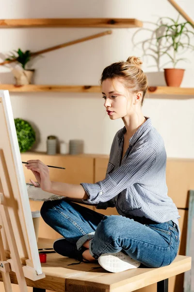 Artiste féminine assise sur la table et dessin image par pinceau — Photo de stock