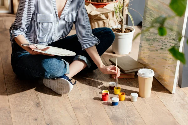 Cropped image of female artist with palette putting brush into paint — Stock Photo