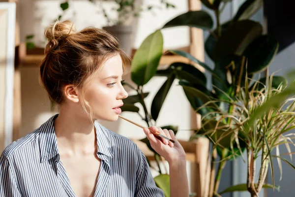 Profil de jeune artiste féminine avec pinceau dans les mains avec des plantes en pot derrière — Photo de stock