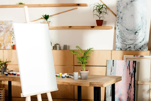 Interno di studio d'artista con cavalletto e tavolo con forniture di pittura e pianta in vaso — Foto stock