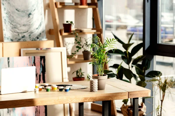 Interno di studio d'artista con forniture di pittura, laptop e piante in vaso — Foto stock