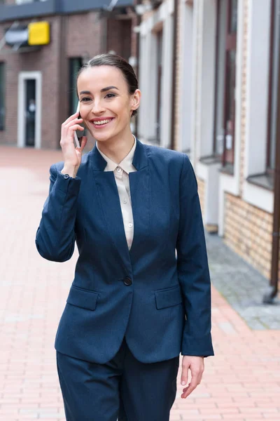 Улыбающаяся красивая деловая женщина разговаривает со смартфоном в городе — стоковое фото