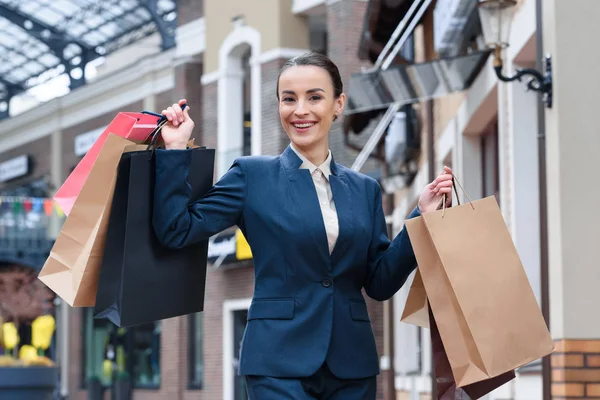 Atractiva mujer de negocios mostrando bolsas de compras y mirando a la cámara — Stock Photo