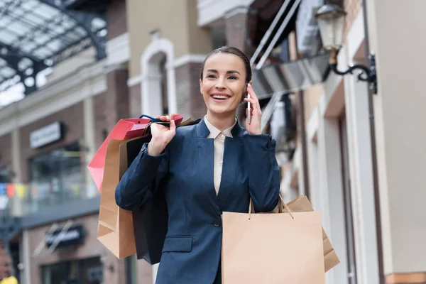 Laughing attractive businesswoman talking by smartphone and holding shopping bags — Stock Photo