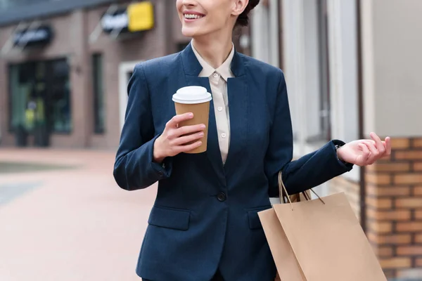 Imagem cortada de empresária segurando café para ir e sacos de compras — Fotografia de Stock