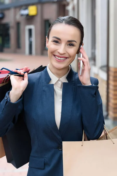 Attractive businesswoman talking by smartphone and holding shopping bags — Stock Photo