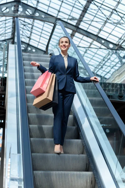 Low angle view of attractive businesswoman standing on escalator with shopping bags — Stock Photo