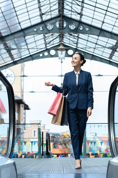 Sonriente atractiva mujer de negocios caminando con bolsas de compras en el centro comercial - foto de stock