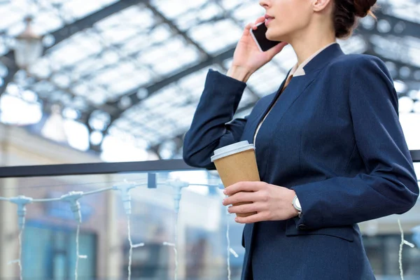 Cropped image of businesswoman talking by smartphone and holding coffee in paper cup — Stock Photo