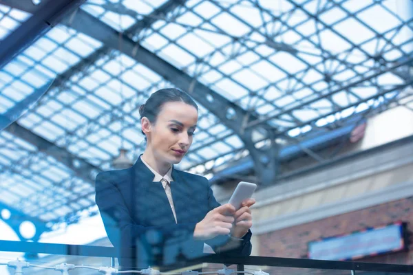 Schöne Geschäftsfrau lehnt sich an Geländer und benutzt Smartphone — Stockfoto