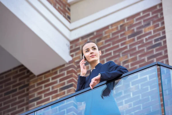 Tiefansicht der schönen Geschäftsfrau, die auf dem Balkon steht und mit dem Smartphone spricht — Stockfoto