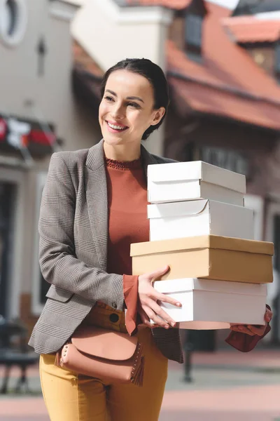 Donna attraente sorridente che tiene scatole della spesa e distoglie lo sguardo — Foto stock