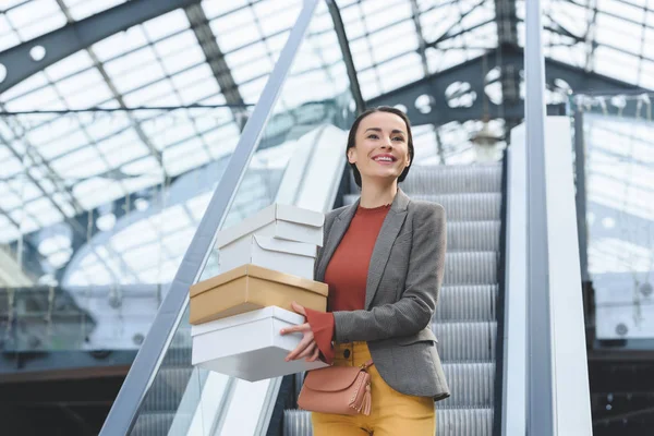 Attractive woman standing on escalator with shopping boxes — Stock Photo