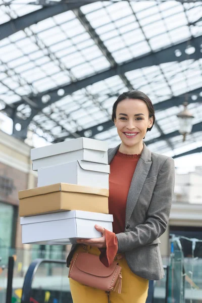 Lächelnde attraktive Frau mit Einkaufskartons, die in die Kamera schaut — Stockfoto