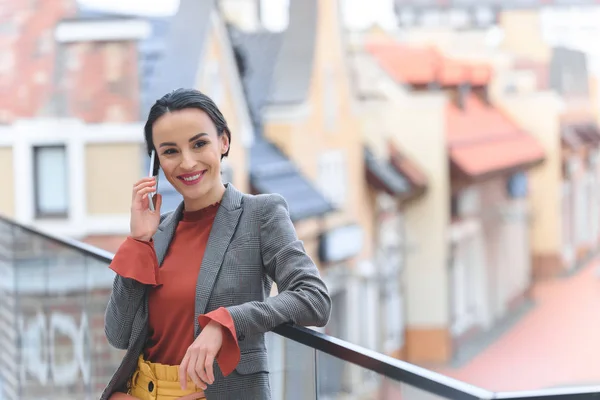 Attraktive, stylische Frau, die auf dem Balkon steht und per Smartphone spricht — Stockfoto