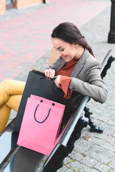 Donna attraente seduta sulla panchina e guardando nella borsa della spesa — Foto stock