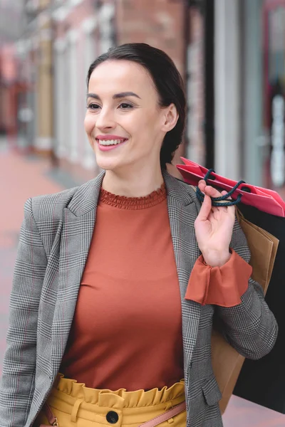 Donna attraente che tiene borse della spesa a spalla e distoglie lo sguardo — Foto stock