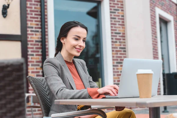 Belle femme élégante en utilisant un ordinateur portable à la table sur la rue — Photo de stock