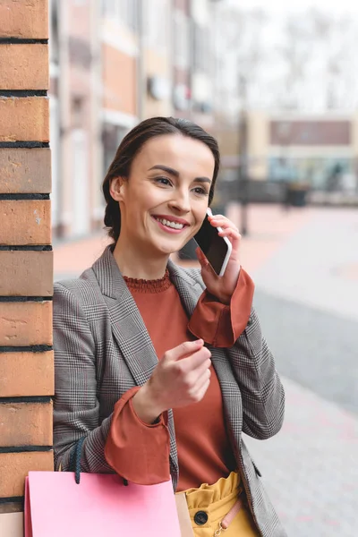 Souriant femme attrayante parler par smartphone et tenant des sacs à provisions — Photo de stock