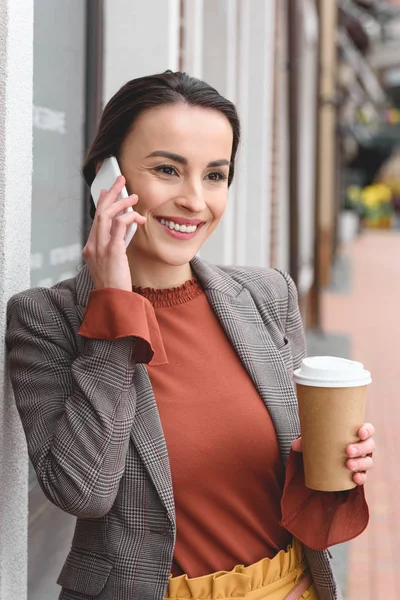 Bela mulher elegante falando por smartphone e segurando café em copo de papel — Fotografia de Stock