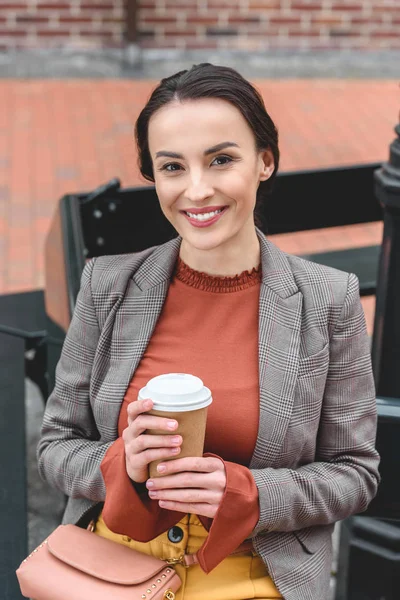 Beautiful stylish woman holding coffee in paper cup and looking at camera — Stock Photo