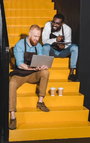 Sonrientes propietarios masculinos de cafeterías en las escaleras con tazas de café - foto de stock