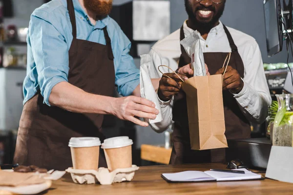Cropped image of owners of coffee shop putting order in paper bag — Stock Photo