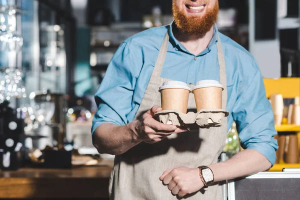 Обрезанное изображение улыбающегося мужчины-баристы с двумя одноразовыми чашками кофе — стоковое фото