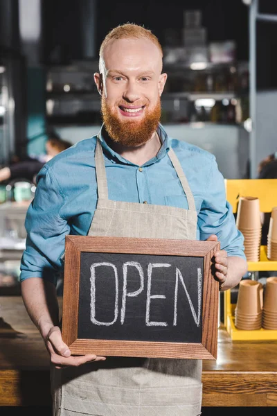 Barista maschio sorridente che tiene la lavagna con scritte aperte in caffetteria — Foto stock