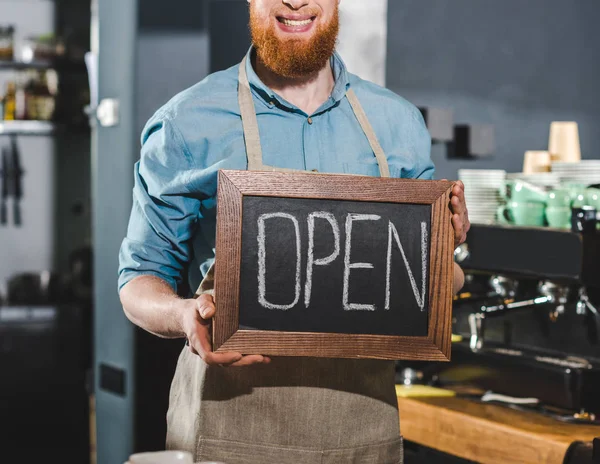 Abgeschnittenes Bild eines jungen männlichen Baristas, der in einem Café eine Tafel mit aufgeklapptem Schriftzug hält — Stockfoto