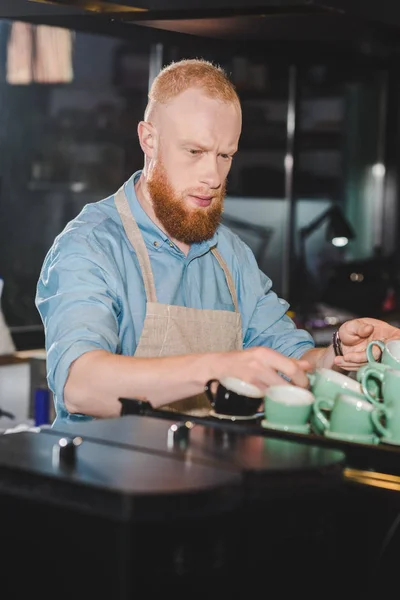 Junge männliche Barista in Schürze nimmt Tassen für Kaffee — Stockfoto