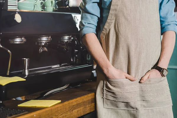 Imagen recortada de barista masculino en delantal de pie cerca de la máquina de café - foto de stock