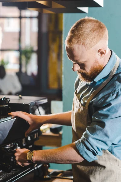 Jovem barista masculino barbudo em avental usando máquina de café — Fotografia de Stock