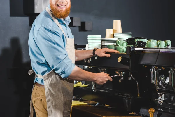 Обрезанное изображение мужчины-баристы в фартуке с помощью кофеварки — стоковое фото