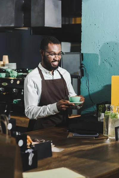 Bonito sorridente africano americano barista em óculos segurando xícara de café no café — Fotografia de Stock