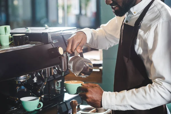 Tiro recortado de sorrir Africano americano barista fazendo cappuccino na máquina de café — Fotografia de Stock