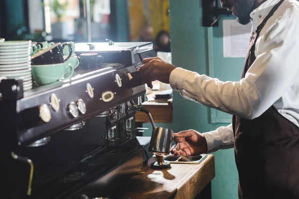 Обрезанный снимок улыбающейся африканской баристы, делающей капучино у кофеварки — стоковое фото