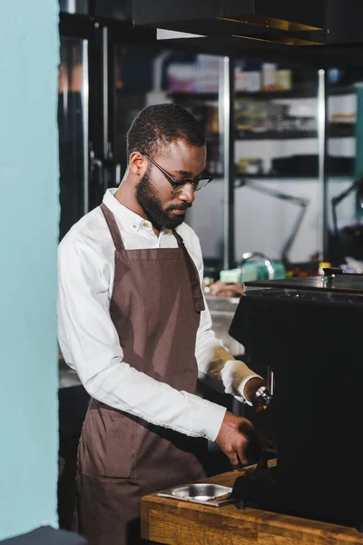 Hübsche junge afrikanisch-amerikanische Barista mit Brille, die Kaffee an der Kaffeemaschine kocht — Stockfoto