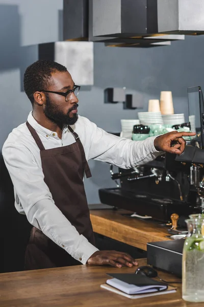 Schöner junger afrikanisch-amerikanischer Barista mit Brille, die auf den Bildschirm zeigt, während er im Café arbeitet — Stockfoto