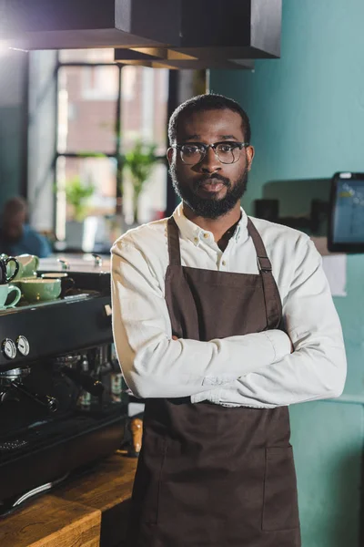 Schöner afrikanisch-amerikanischer Barista, der mit verschränkten Armen im Café steht und in die Kamera schaut — Stockfoto