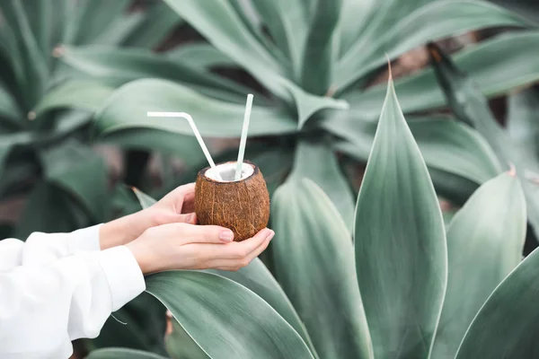 Abgeschnittene Ansicht einer Frau mit frischem Cocktail in Kokosnuss mit Strohhalmen, auf tropischem Hintergrund — Stockfoto