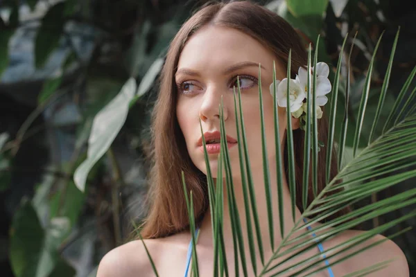 Beautiful young woman posing with palm leaf on tropical resort — Stock Photo