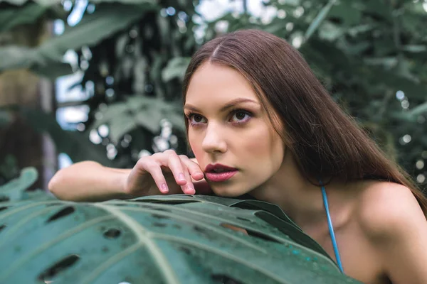 Hermosa chica posando en jardín tropical cerca de hoja de monstera - foto de stock