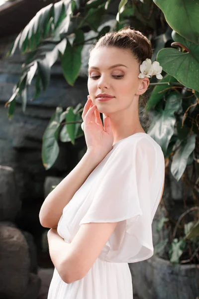 Noiva atraente em vestido branco com flor no cabelo posando no jardim tropical — Fotografia de Stock