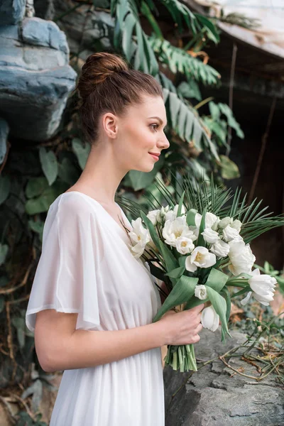 Modische Braut posiert im weißen Kleid mit Brautstrauß — Stockfoto