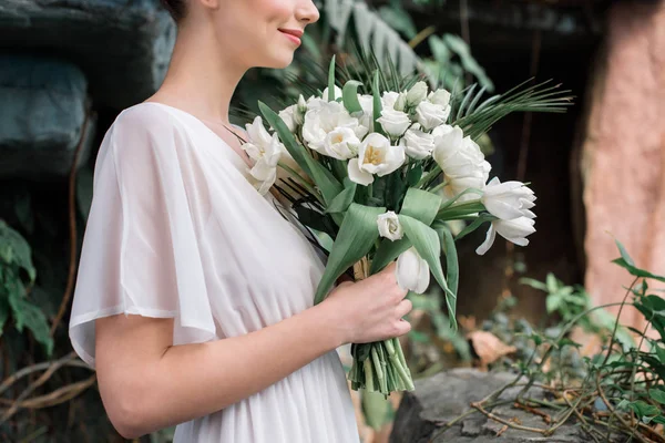 Обрезанный вид невесты в белом платье со свадебным букетом — стоковое фото