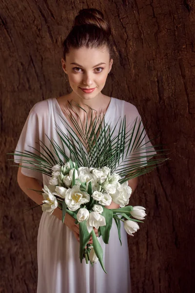 Attraente giovane donna in abito bianco in posa con bouquet da sposa — Foto stock